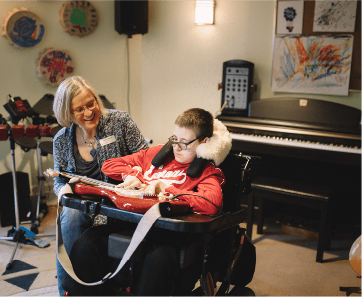 Woman helping young boy in wheel chair with playing the guitar