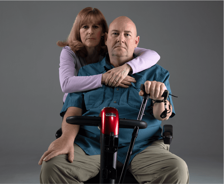 Man with ALS sitting in scooter with woman embracing him from behind
